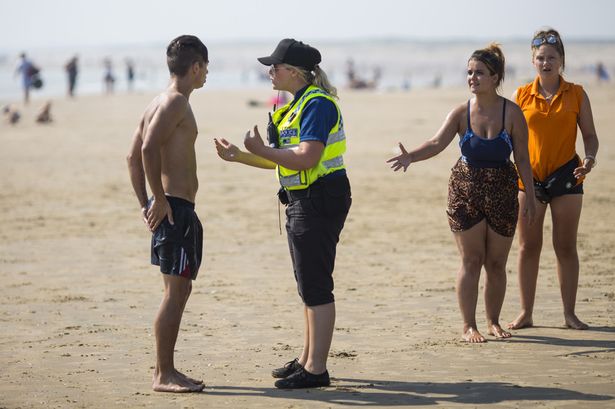 A police officer advises a swimmer to come in as the tide moves in on Camber Sands