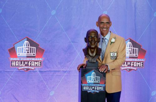 Tony Dungy in beige suit next to brown metal bust of his head