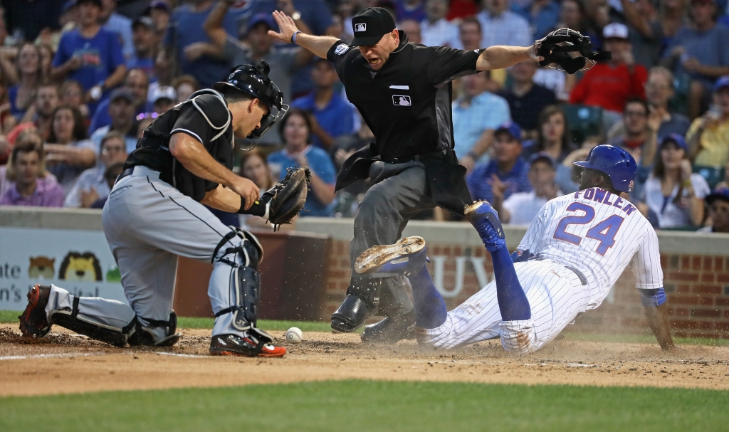 Home plate umpire Mike Muchlinski #76 signals that Dexter Fowler #24 of the Chicago Cubs is safe at home plate after J.T. Realmuto #11 of the Miami Marlins dropped the ball on the tag attempt in the 3rd inning at Wrigley Field