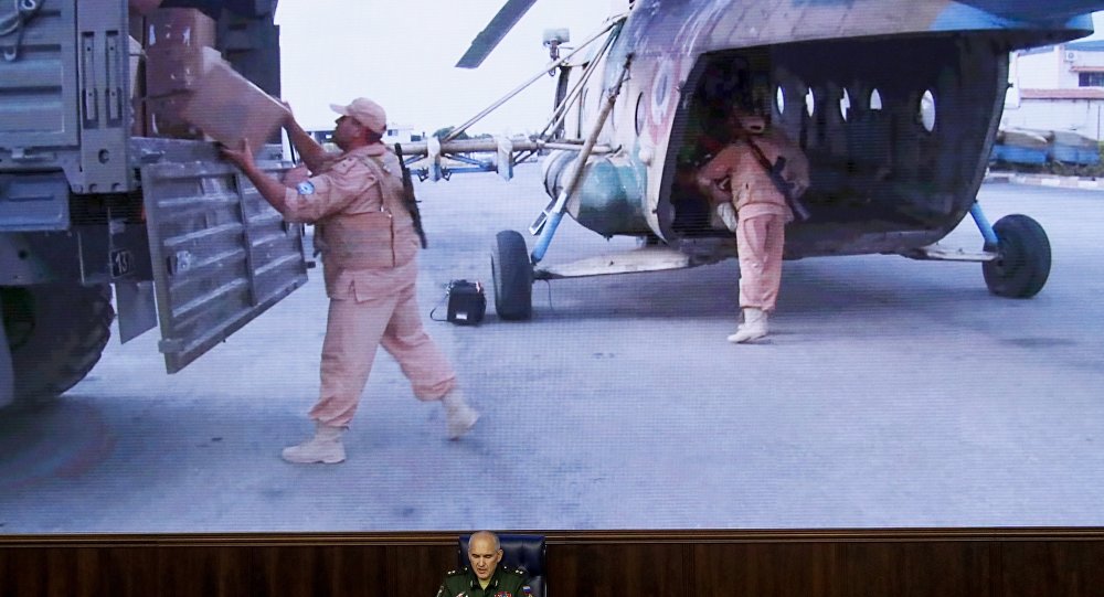 Lt.-Gen. Sergei Rudskoi of the Russian Military General Staff speaks to the media as Syrian army soldiers load a humanitarian aid at Aleppo is displayed on screen at a Russian Defense Ministry building in Moscow Russia Monday Aug. 1 2016