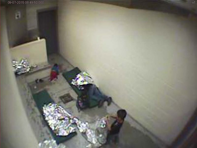 This September 2015 image made from U.S. Border Patrol surveillance video shows a child crawling on the concrete floor near the bathroom area of a holding cell and a woman and children wrapped in Mylar sheets at a U.S. Customs and Border Protection sta