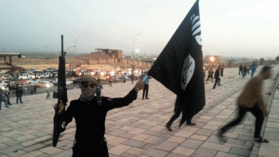 A fighter of the Islamic State of Iraq and the Levant holds an ISIL flag and a weapon on a street in the city of Mosul on 23 June 2014