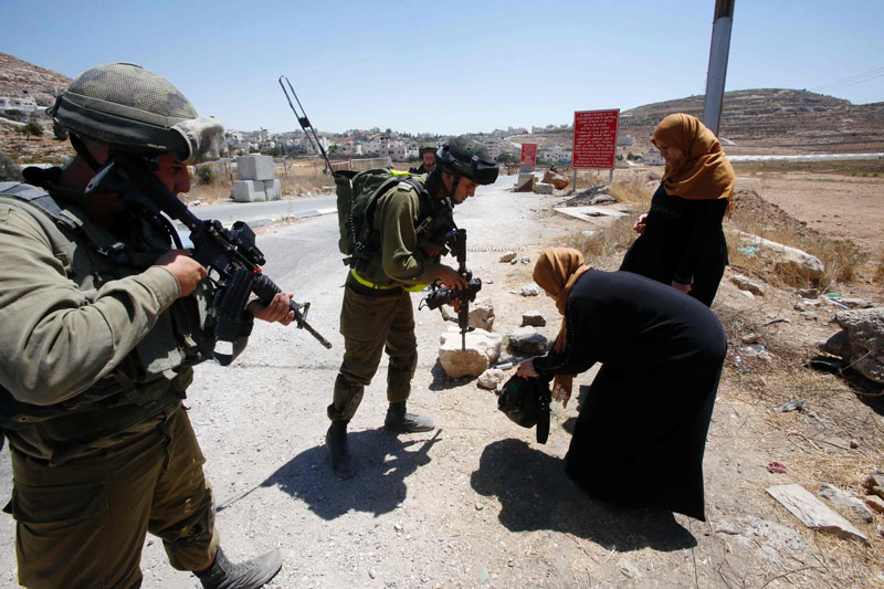 Israeli soldiers control Palestinians at an entrance of the al Fawwar refugee camp south of the West Bank city of Hebron