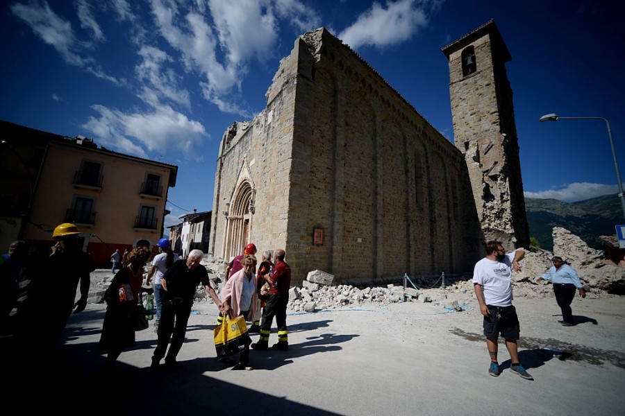 People walk past an earthquake damaged church during search and rescue operations in Amatrice