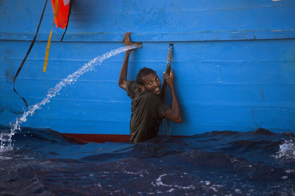 A man holds himself on the side of a boat after jumping into the sea from a crowded wooden boat during the rescue operation