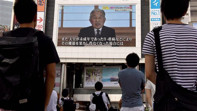 People look at a big video screen on the street as a speech by Japanese Emperor Akihito to the nation is televised in Tokyo