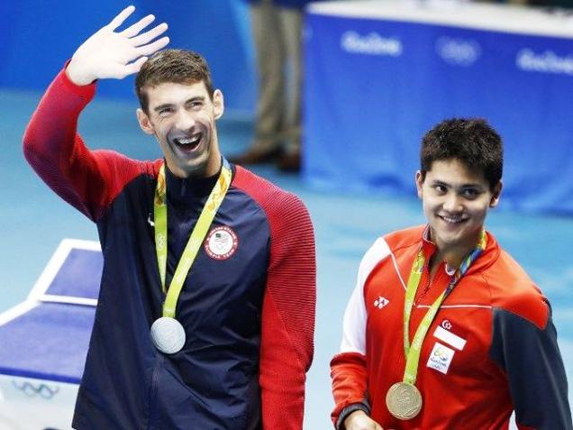 Silver medallist Michael Phelps waves next to gold medallist Singapore's Schooling Joseph during the medal ceremony of the men's 100m Butterfly final at the Rio 2016 Olympic Games in Rio de Janeiro on Friday