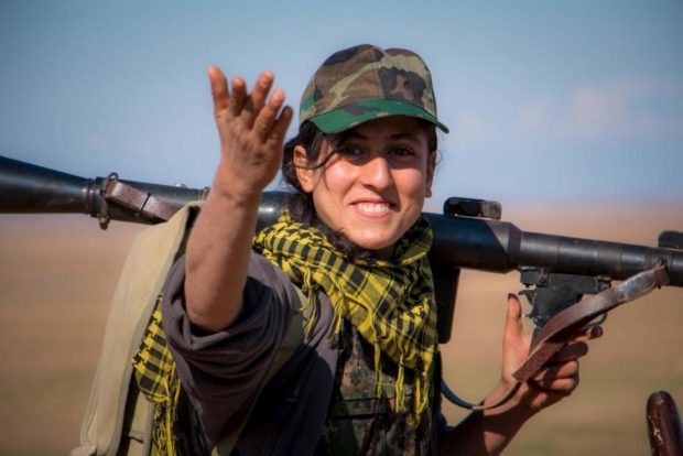 A Kurdish female fighter from the People's Protection Units gestures as she carries her weapon near al Hawl area in the southeastern city of Hasakah Syria