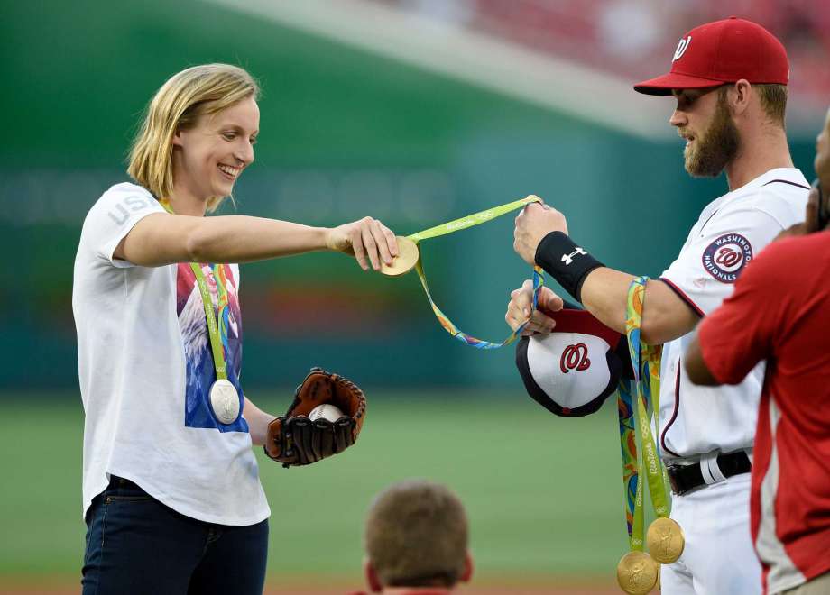 Olympic gold medal swimmer Katie Ledecky left hands her medals to Washington Nationals Bryce Harper right to hold before she threw out the ceremonial first pitch before a baseball game between the Baltimore Orioles and the Washington Nationals Wedne