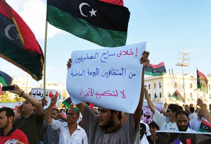 Libyans wave their national flag and hold a poster reading in Arabic 'Release the protestors arrested last Friday. Do not silence us&#039 during a demonstration in Tripoli's Martyrs&#039 Square against French military intervention in Libya