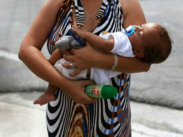 MIAMI FL- AUGUST 02 Barbara Betancourt holds her baby Daniel Valdes after being given a can of insect repellent by James Bernat a City of Miami police officer as he helps people living around the Miami Rescue Mission prevent mosquito bites that may