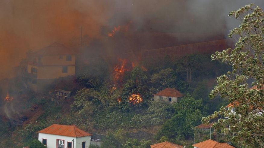 A forest fire rages near houses in Curral dos Romeiros on the outskirts of Funchal the capital of the Madeira island Portugal Tuesday Aug. 9 2016. Flames from forest fires licked at homes around Funchal casting a smoke plume over the downtown and for