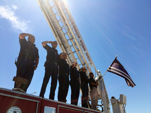 Albuquerque firefighters salute as law enforcement officers escort the body of a New Mexico police officer who was shot and killed during a traffic stop as