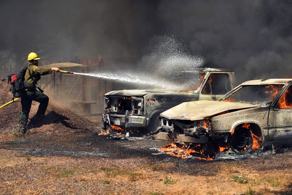 A Cal Fire firefighter douses burning cars as they burn in the town of Lower Lake Calif. on Sunday Aug. 14 2016. Flames continue to burn out of control in the area. The fire was creating its own weather pattern and shifted northward into Lower Lake