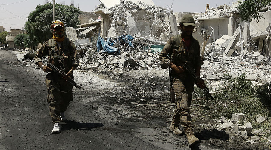 Members of the Syrian Democratic Forces walk past collapsed buildings in the northern Syrian town of Manbij