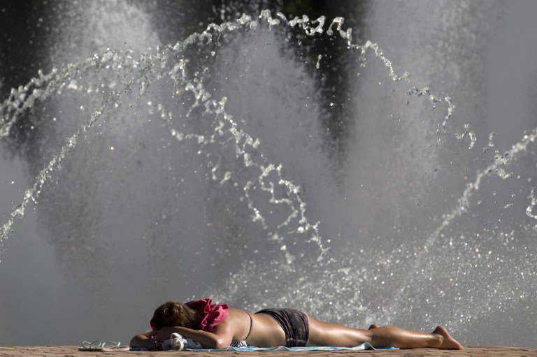 A woman sunbathes next to water fountains in Battersea Park in London