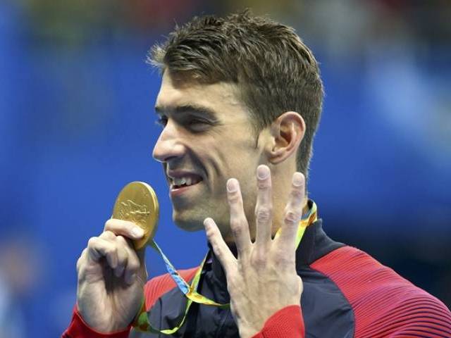 Michael Phelps gestures to indicate the four gold medals he has won at this Olympic Games as he poses with his gold medal