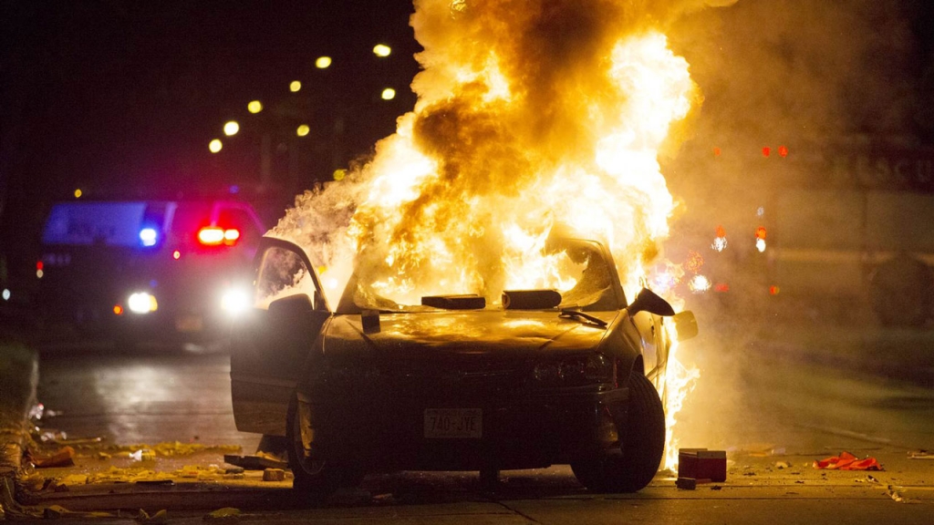 A car burns as a crowd of more than 100 people gathers following the fatal shooting of a man in Milwaukee Saturday Aug. 13 2016