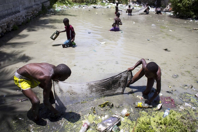 Young boys look for fish in a basin of polluted water in Delmas a neighborhood of Port-au-Prince Haiti Friday Aug. 19 2016. Haiti is the poorest country