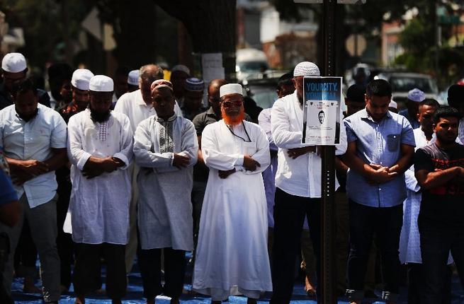 A sketch of a suspect is secured to a post as men pray outside of the Al Furqan Jame Masjid mosque where Imam Maulama Akonjee and his assistant Thara Uddin 64 were killed in a shooting on August 13 in the Queens borough of New York