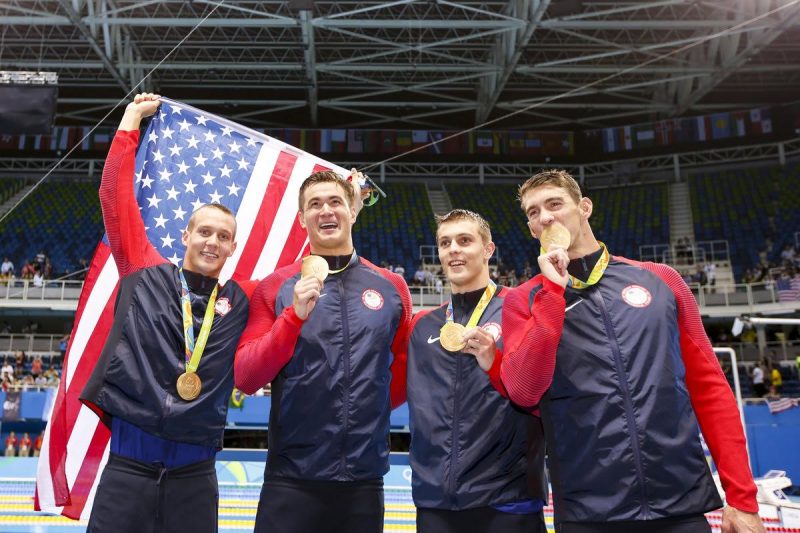 Caeleb Dressel Nathan Adrian Ryan Held and Michael Phelps of the United States of America pose with their Gold medals and a US flag after winning in the men's 4x100m Freestyle Relay Final- by Patrick B. Kraemer