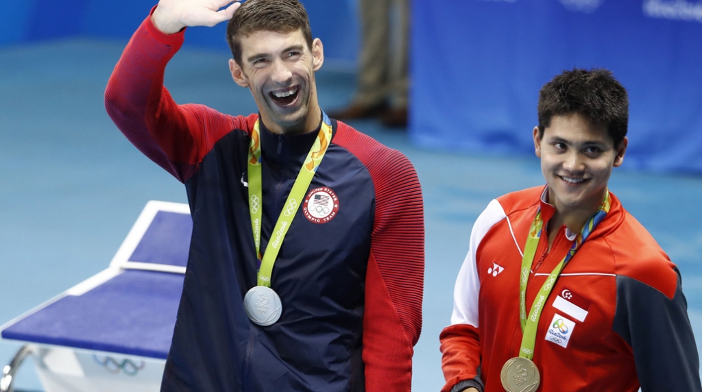 Silver medallist USA's Michael Phelps waves nex to gold medallist Singapore's Schooling Joseph during the medal ceremony of the Men's 100m Butterfly Final during the swimming event at the Rio 2016 Olympic Games at the Olympic Aquatics S