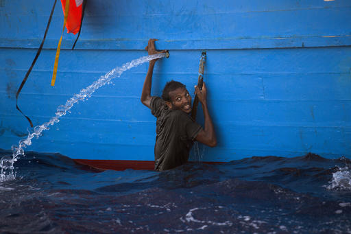 A man holds himself on the side of a boat after jumping into the sea from a crowded wooden boat during a rescue operation at the Mediterranean sea about 13 miles north of Sabratha Libya Monday Aug. 29 2016