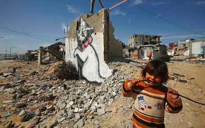 A Palestinian girl looks on as a mural of a kitten is seen on the remains of a house that witnesses said was destroyed by Israeli shelling during a 50-day war in Biet Hanoun town in the northern Gaza Strip