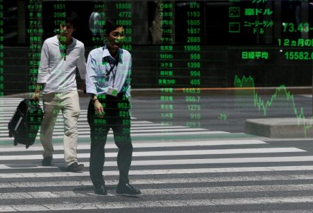 Passersby are reflected on a stock quotation board outside a brokerage in Tokyo Japan