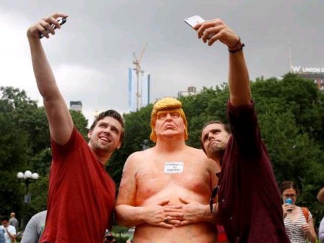 People pose for selfies with a naked statue of Donald Trump that was left in Union Square Park in New York City