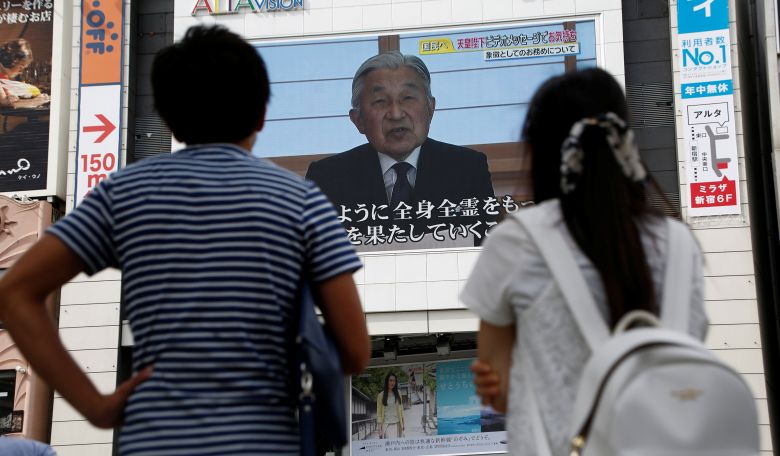 People watch a large screen showing Japanese Emperor Akihito's video address in Tokyo Japan