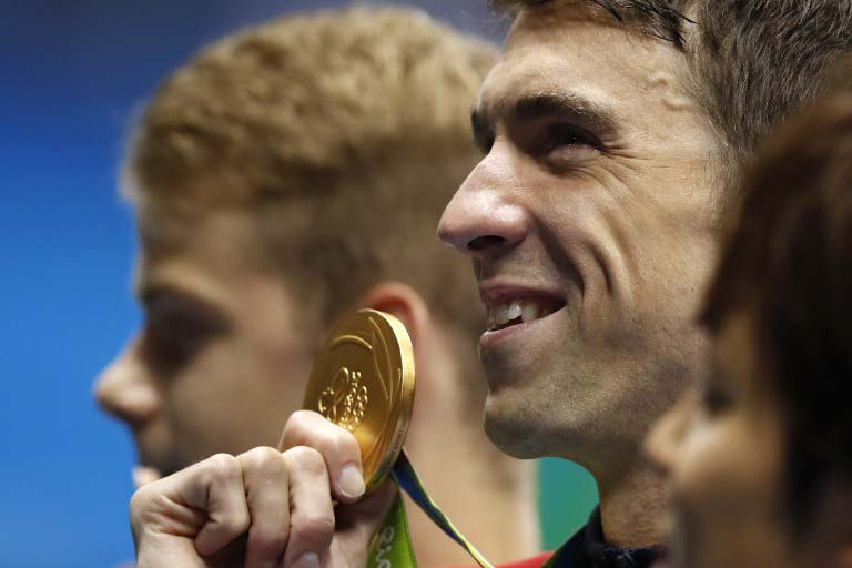 USA's Michael Phelps poses with his gold medal on the podium after he won the Men's 200m Butterfly Final during the swimming event at the Rio 2016 Olympic Games at the Olympic Aquatics Stadium in Rio de Janeiro