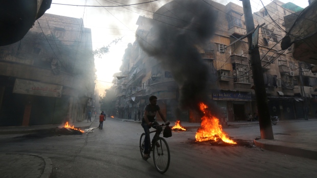 A man in Aleppo rides a bicycle past burning tires on Aug. 1 2016. Activists say they are used to create smoke cover from war planes