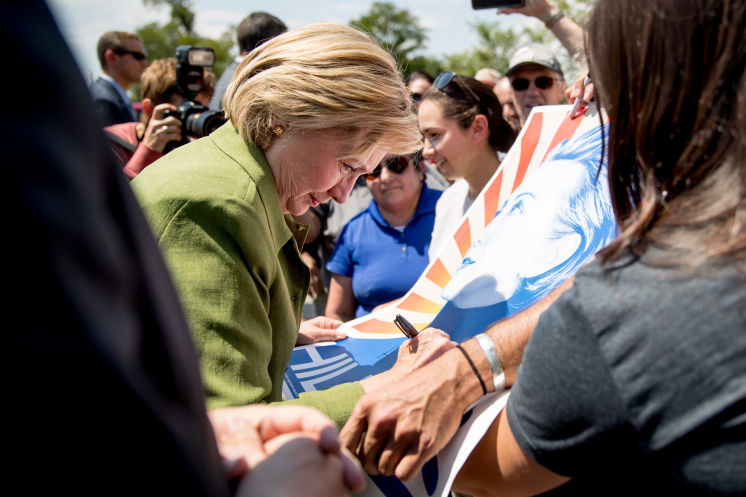 Democratic presidential candidate Hillary Clinton signs a poster Wednesday after touring the Knotty Tie Company in Denver where she criticized Donald Trump for hurting small businesses