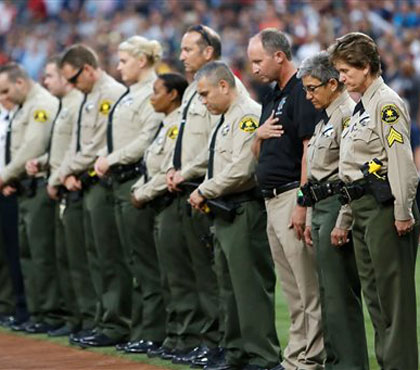 San Diego County Sheriff's Department officers stand in memory of officer Jonathan De Guzman with a moment of silence before a baseball game between the Cincinnati Reds and the San Diego Padres on Friday