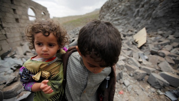 A boy carries his sister as he walks on rubble of a houseafter it was destroyed by a Saudi-led air strike in Yemen's