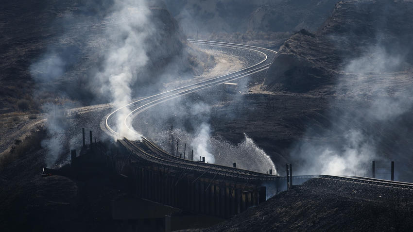 Smoke rises from beneath railroad tracks damaged by the Blue Cut Fire