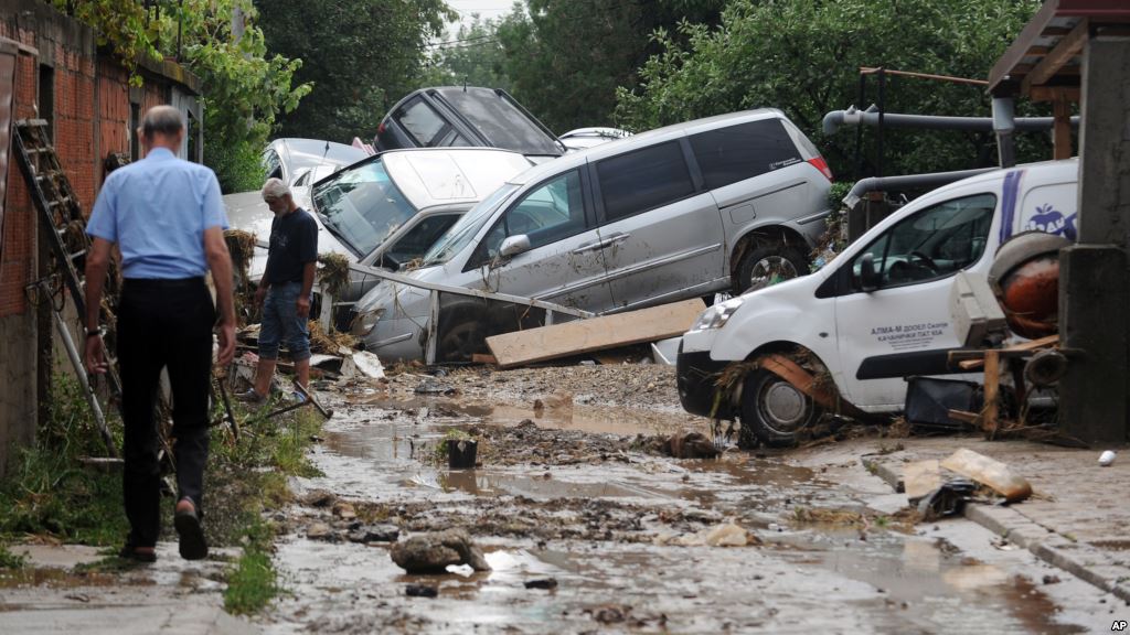 People walk through a street where cars have piled due to overnight flooding after storms in the village of Stajkovci just east of Skopje Macedonia Aug. 7 2016