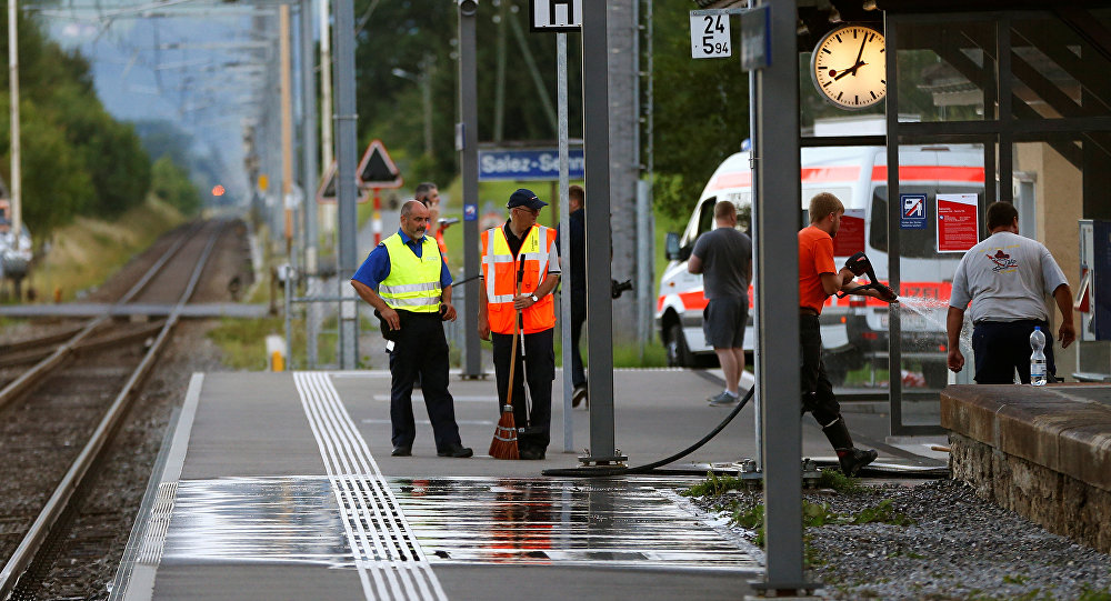 A Swiss police officer stands near workers cleaning a platform after a 27-year-old Swiss man's attack on a Swiss train at the railway station in the town of Salez Switzerland