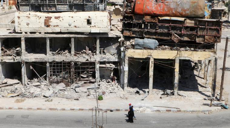 People walk past damaged buses positioned atop a building as barricades in the rebel-held Bab al Hadid neighbourhood of Aleppo Syria