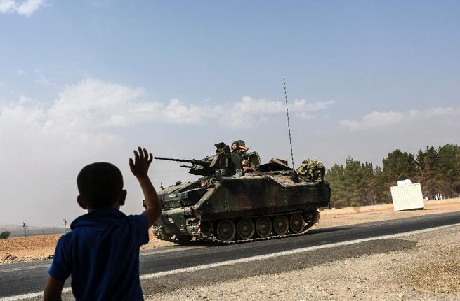 A Turkish boy waves to Turkish tank convoy driving into Syria from the border city of Karkamis in the southern region of Gaziantep