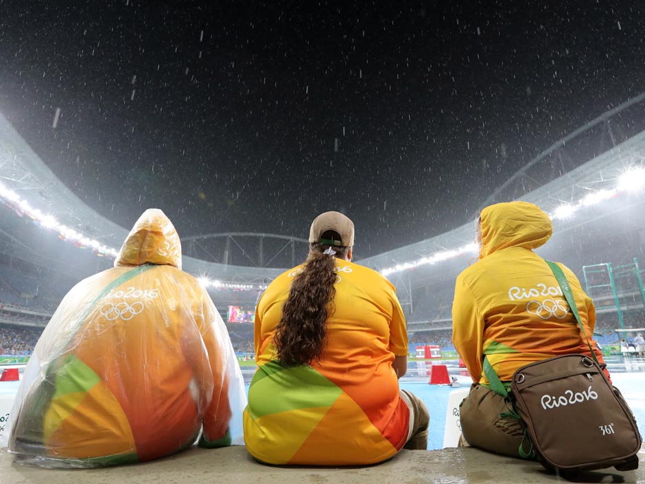 Olympic volunteers sit in the rain during the athletics competitions of the Summer Olympics at the Olympic Stadium in Rio de Janeiro Brazil on Monday Aug. 15 2016