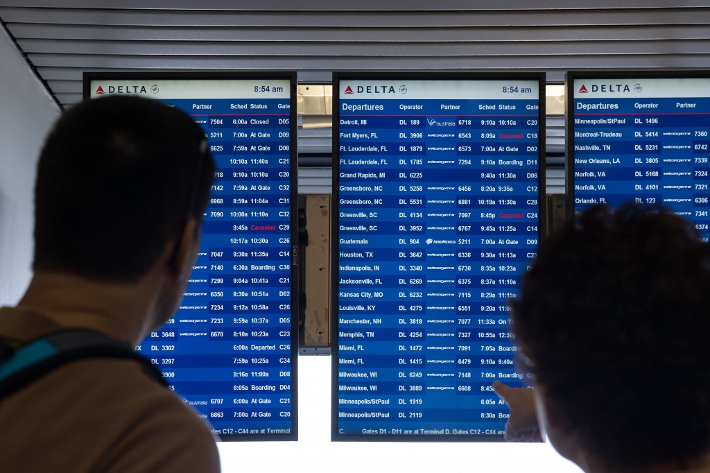 Travelers check the Delta departures board at La Guardia Airport