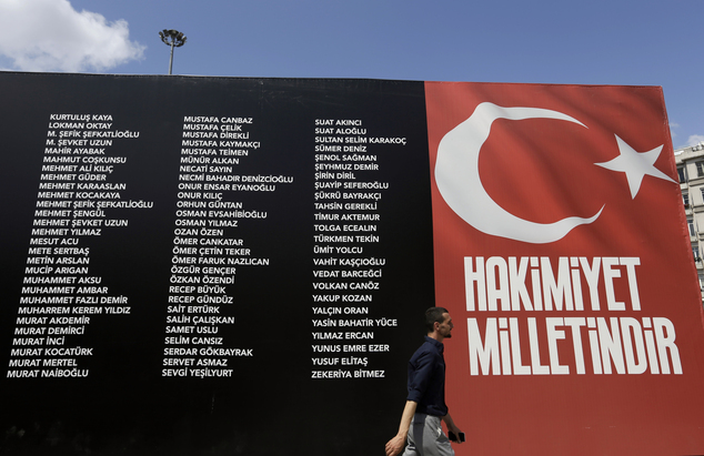 A pedestrian passes a sign commemorating people who died fighting the July 15th coup as the banner with the Turkish flag reads''Sovereignty belongs to the