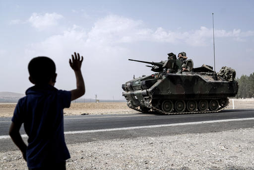 A child waves toward Turkish troops heading to the Syrian border in Karkamis Turkey Friday Aug. 26 2016. Turkey's state-run Anadolu news agency said late Thursday Turkish artillery have shelled a group of Syrian Kurdi