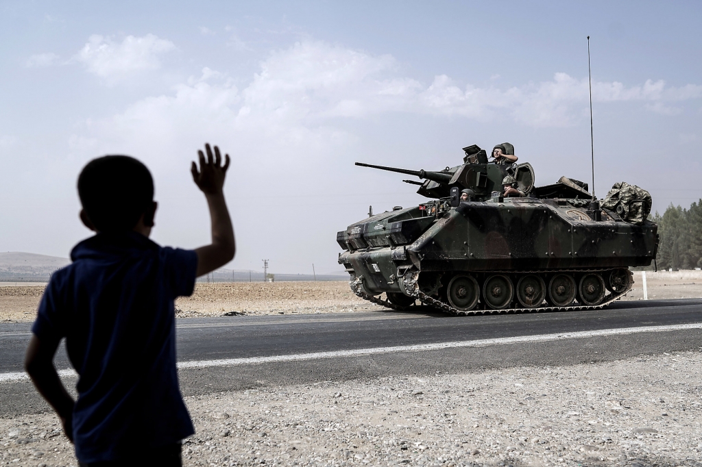 A child waves toward Turkish troops heading to the Syrian border in Karkamis Turkey Friday Aug. 26 2016. Turkey's state-run Anadolu news agency said late Thursday Turkish artillery have shelled a group of Syrian Kurdish militia fighters in the