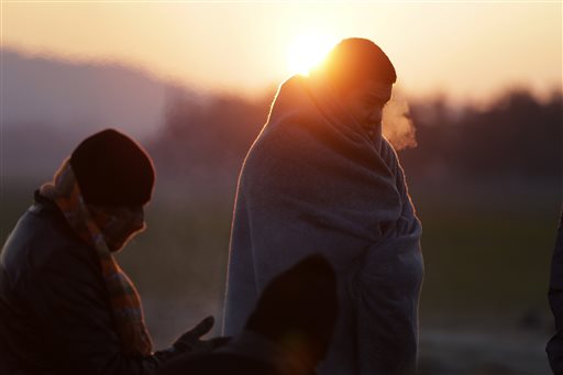 Refugees try to warm up around a fire as the sun rises at a refugee camp in the northern Greek village of Idomeni Thursday Jan. 21 2016. About 1,000 refugees from Syria Afghanistan and Iraq are stranded at Greece's northern border with Macedonia