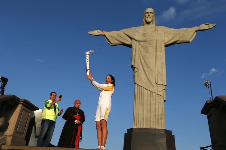 Rio Olympics- Olympic torch- Rio de Janeiro Brazil 05/08/2016. Former Brazilian volleyball player Isabel Barroso holds the Olympic torch next to Christ the Redeemer statue watched by Rio Mayor Eduardo Paes and archbishop Orani Joao Tempesta. REUTER