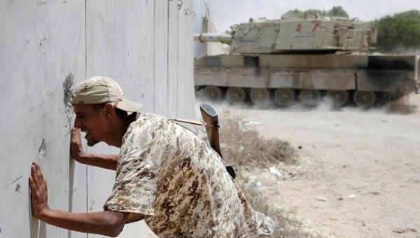 A fighter of Libyan forces looks through a hole in a wall as a self-propelled artillery gun fires at Islamic State fighters during a battle in Sirte Libya