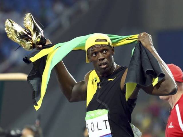 Usain Bolt carries his shoes in his hands after winning the gold medal